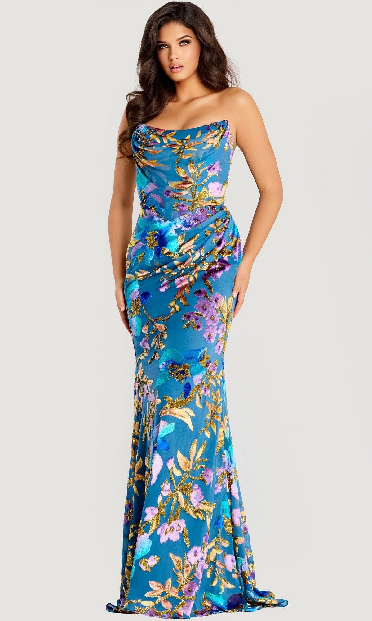 A woman poses in the Jovani 47654 long prom dress, featuring a fitted, strapless design with a vibrant floral print on a blue background—perfect for making a statement at your next event.